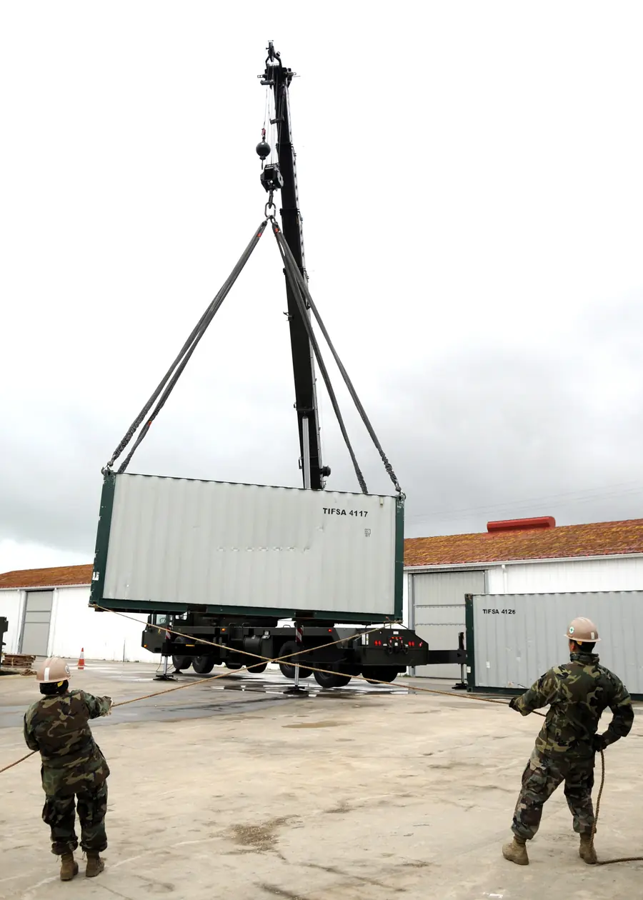 Two riggers holding tag lines below a container suspended from a crane