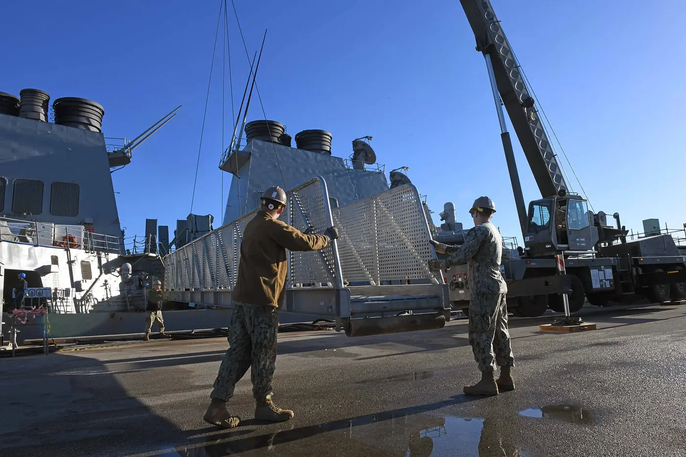 Two riggers steadying a suspended load with a tag line while a crane holds it
